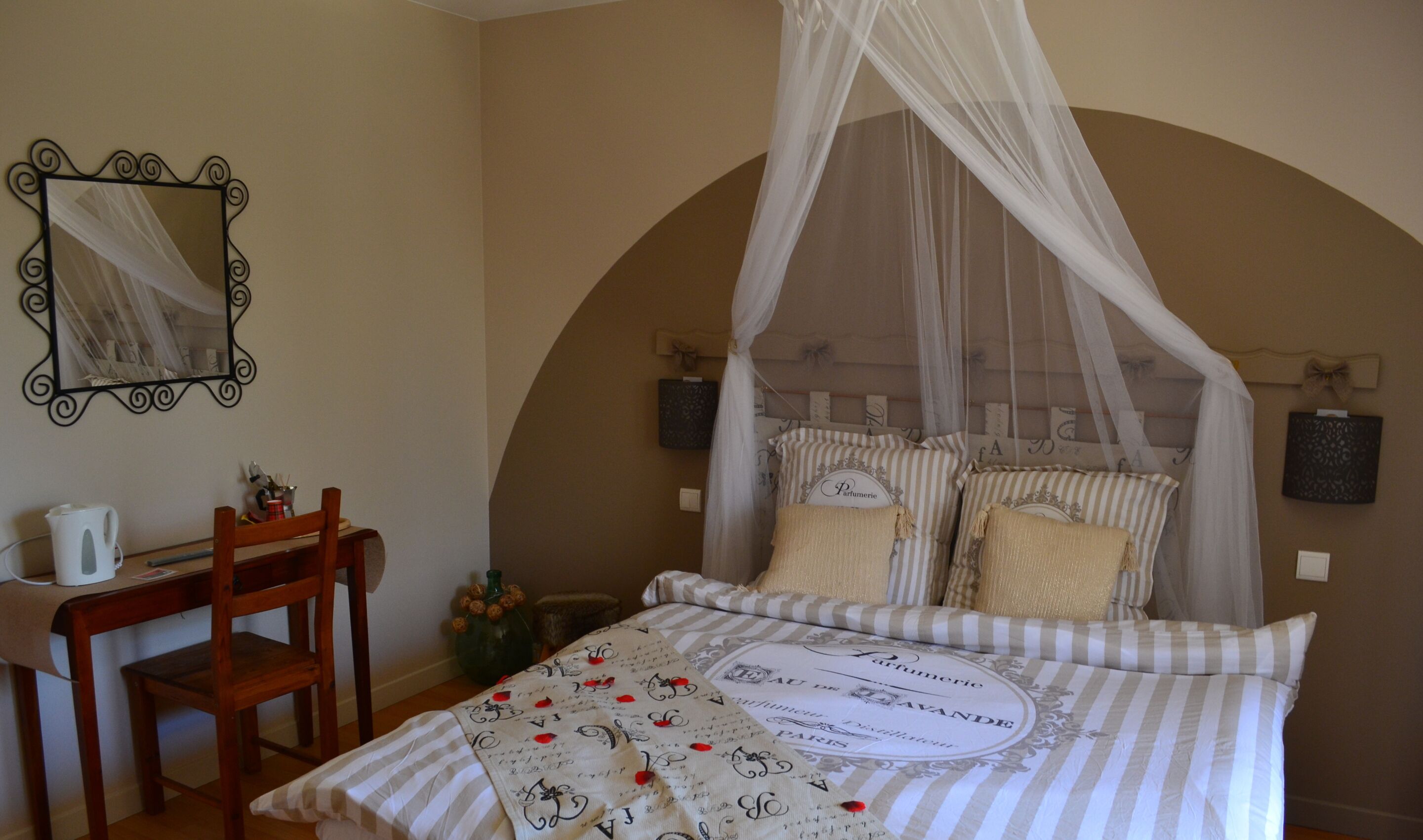 Une chambre à coucher avec un lit à baldaquin, une chaise, une table de chevet avec une lampe et un miroir au mur.