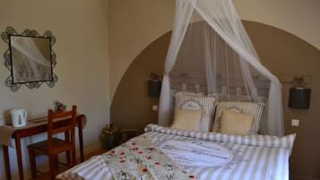 Un dormitorio con cama con dosel, una silla, una mesita de noche con lámpara y un espejo en la pared.