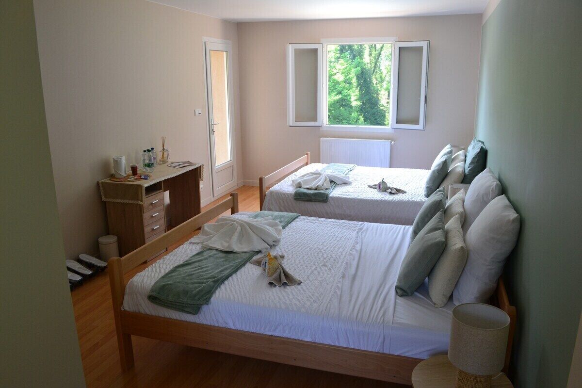 Een slaapkamer met twee bedden, een bureau en een raam met uitzicht op groen.