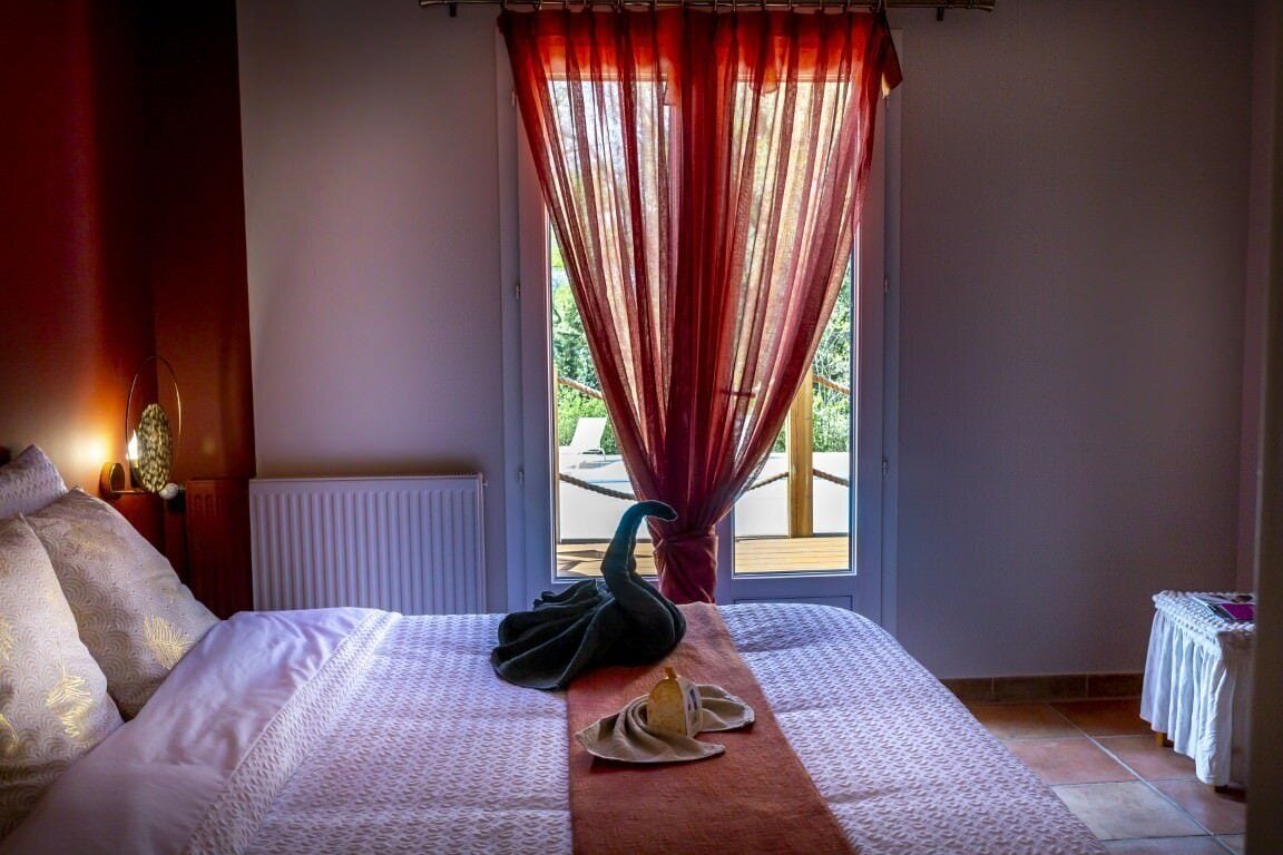 Habitación de hotel con cama, almohada con forma de cisne, toalla con forma de cisne y ventana con vistas a zonas verdes.