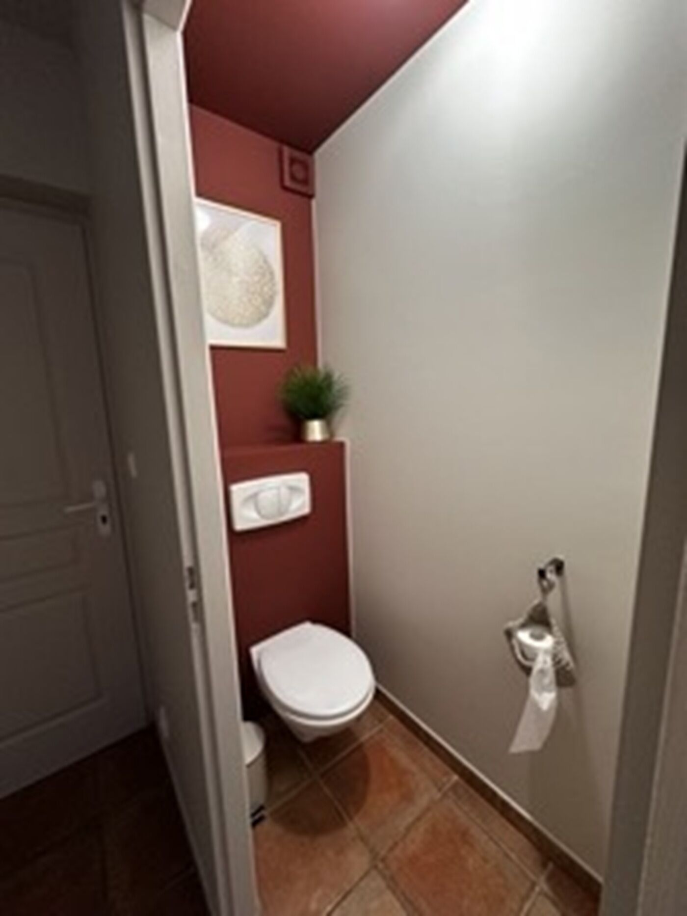 Une petite salle de bain aux dimensions réduites, avec des toilettes blanches, un petit lavabo et une plante en pot accrochée au mur.