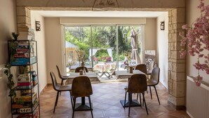 A dining area with a stone archway, a bookshelf with board games, and a view of the garden through large glass doors. - Douceur Des Mées (Les Mees)