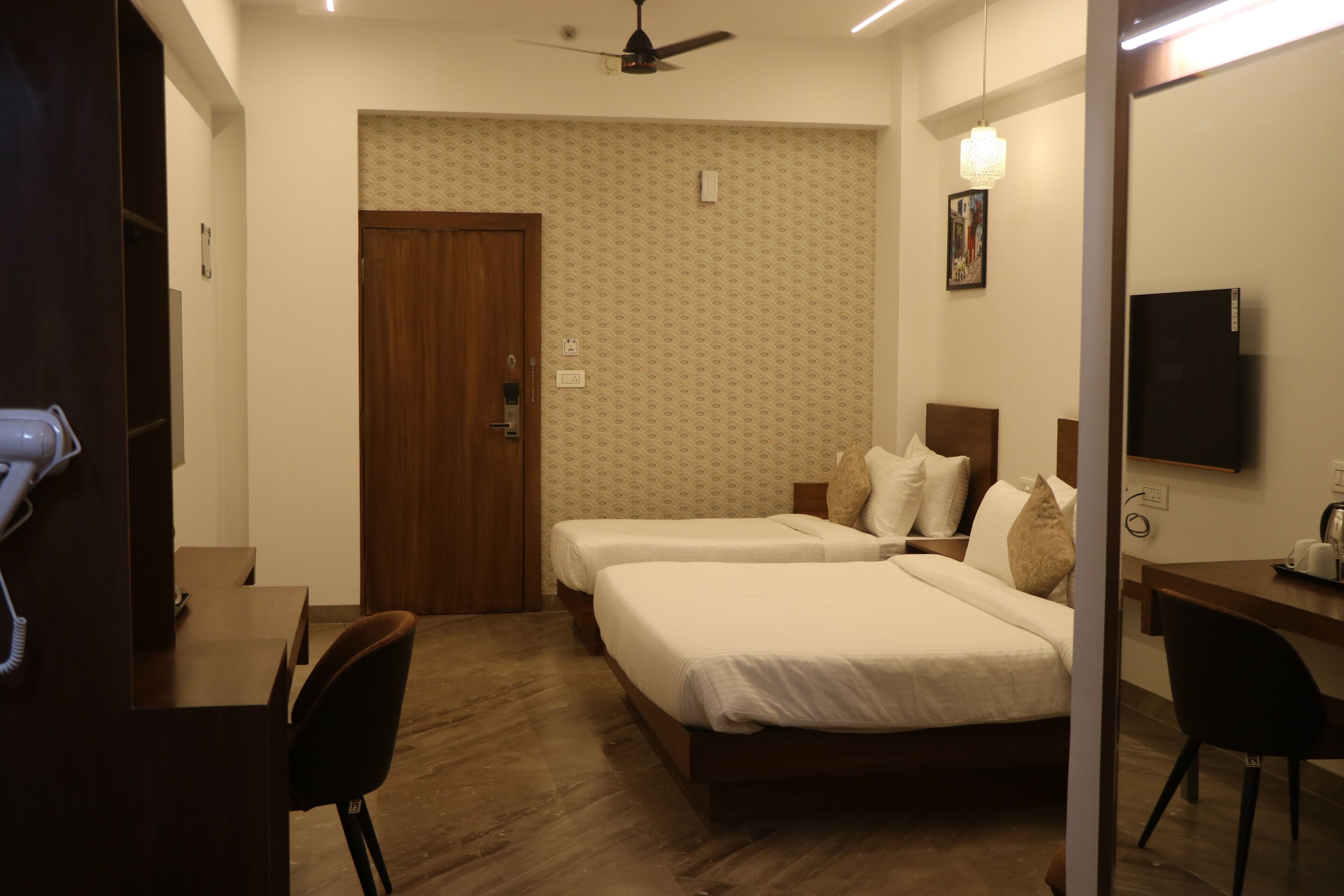 Habitación de hotel con dos camas, un escritorio, una silla, un armario y un televisor.