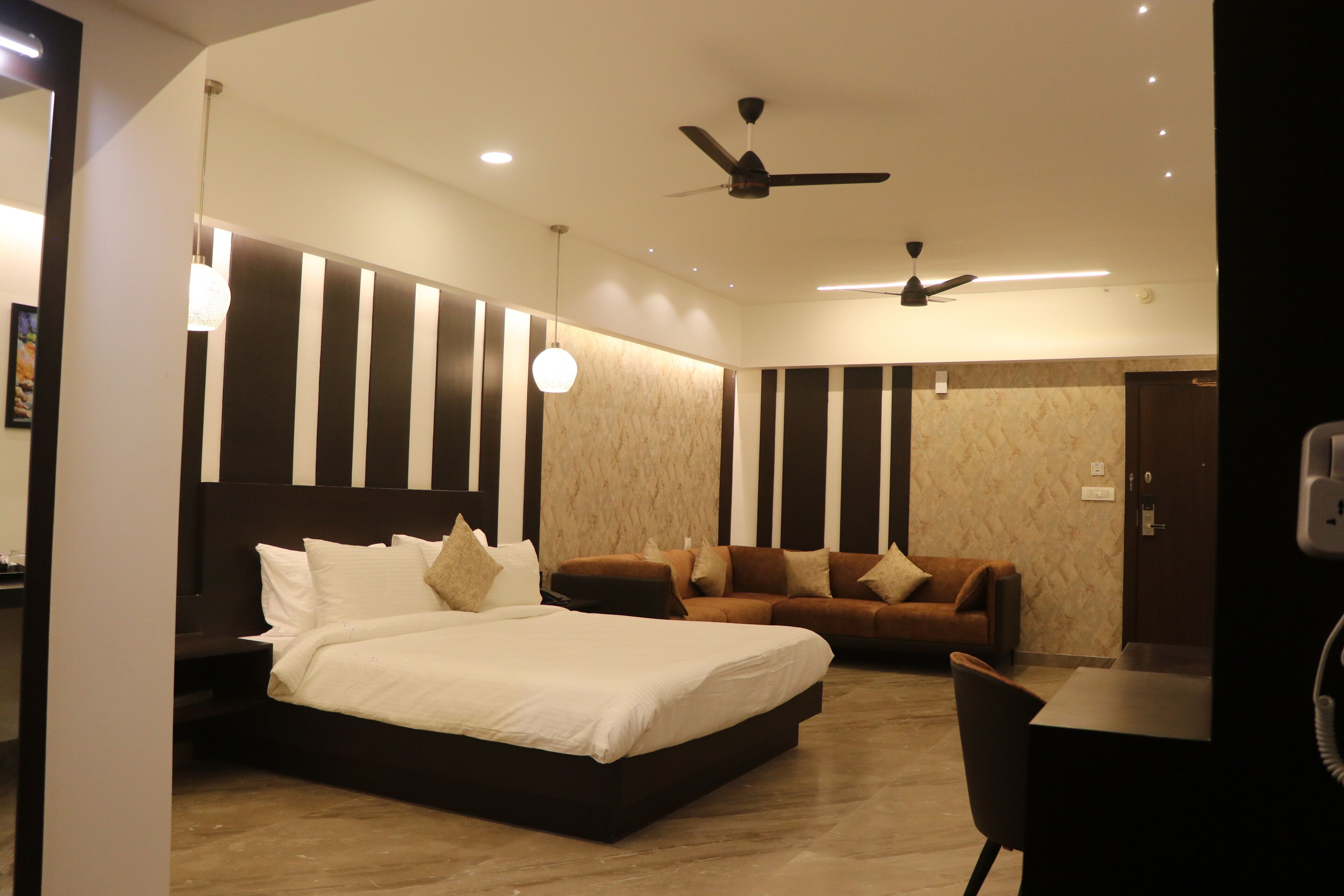 A modern hotel room with a large bed, a sofa, a desk, and a ceiling fan.