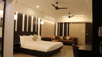 A modern hotel room with a large bed, a sofa, a desk, and a ceiling fan.