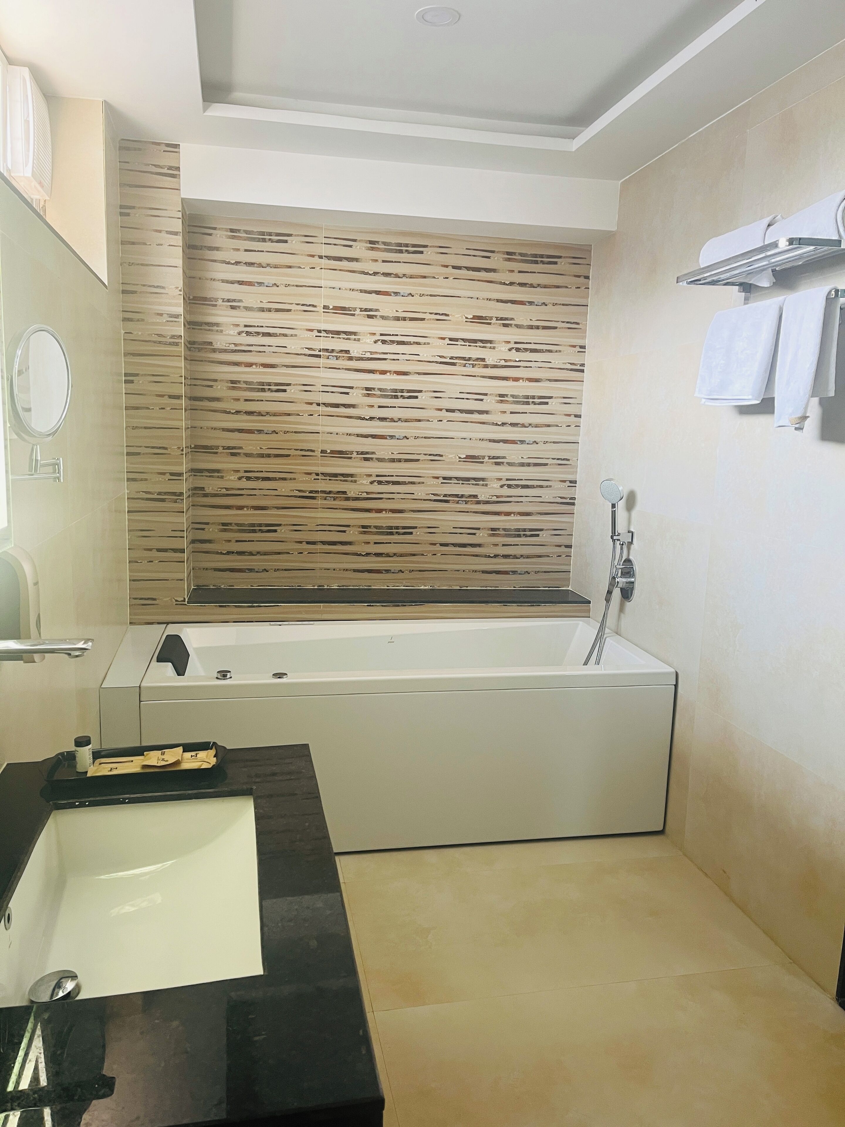Een moderne badkamer met een groot bad, een zwart aanrecht met een wastafel en een houten wandpaneel.