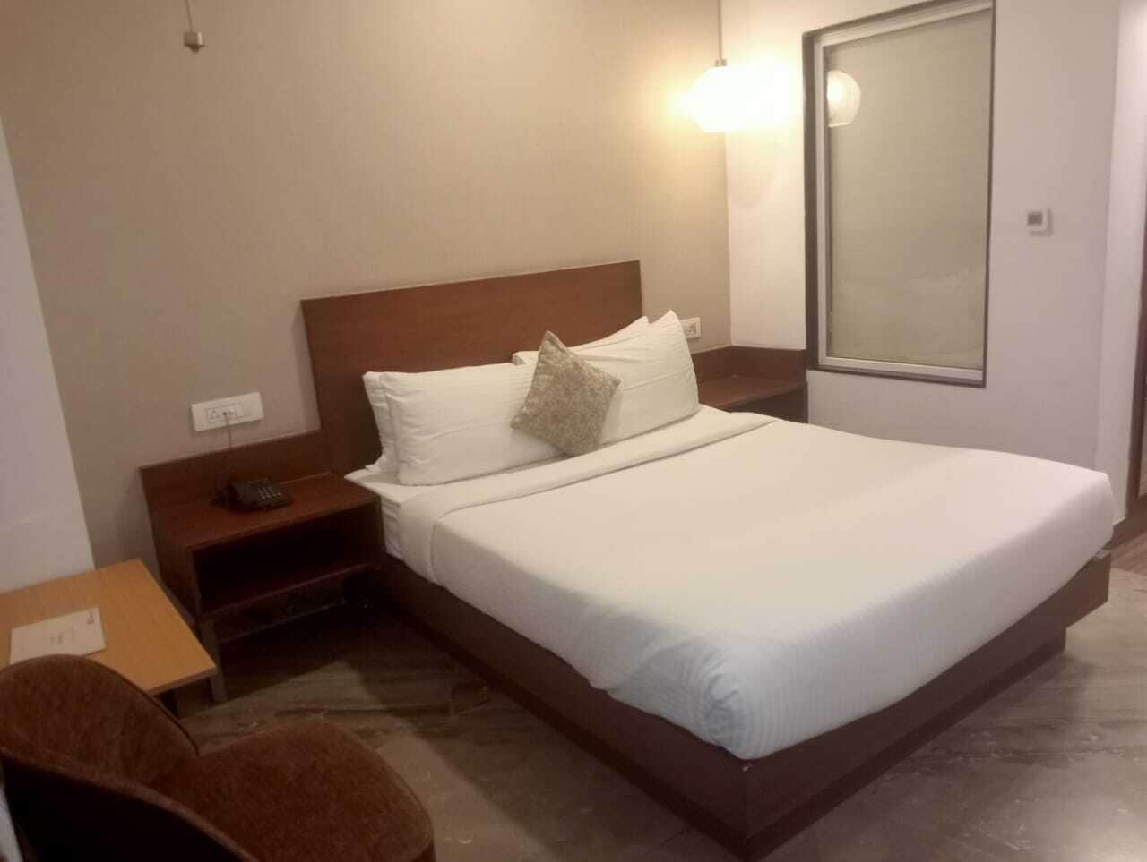 A hotel room with a large bed, a nightstand, a chair, and a mirror.