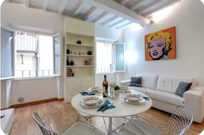 A dining area with a round table set for four, surrounded by metal chairs. A white sofa is positioned against the wall, and a colorful pop art painting is displayed above it. - Central and Prime Apartment Near Duomo (Florence)
