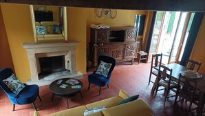 Ein Wohnzimmer mit Kamin, einem gelben Sofa, blauen Sesseln und einem Essbereich mit Holztischen und -stühlen.