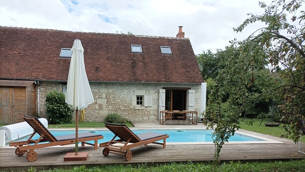 Ein Poolbereich mit zwei Liegestühlen, einem Tisch und einem Sonnenschirm.