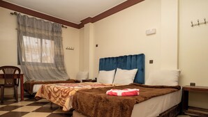 Una habitación de hotel con piso a cuadros, una cama con cabecera marrón, una silla y una ventana con cortinas translúcidas.