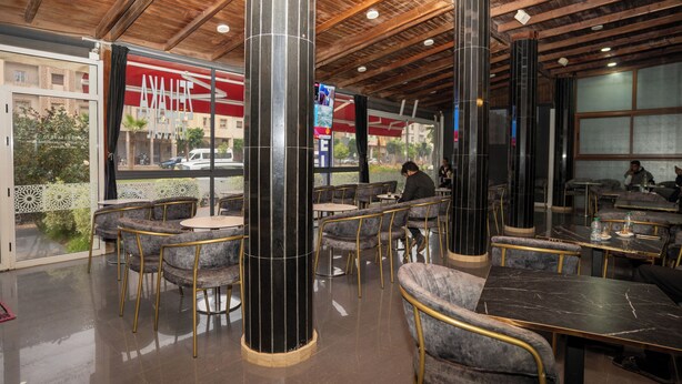 Un restaurante con una decoración moderna, que presenta columnas de mármol negro, asientos acolchados y un techo de madera.