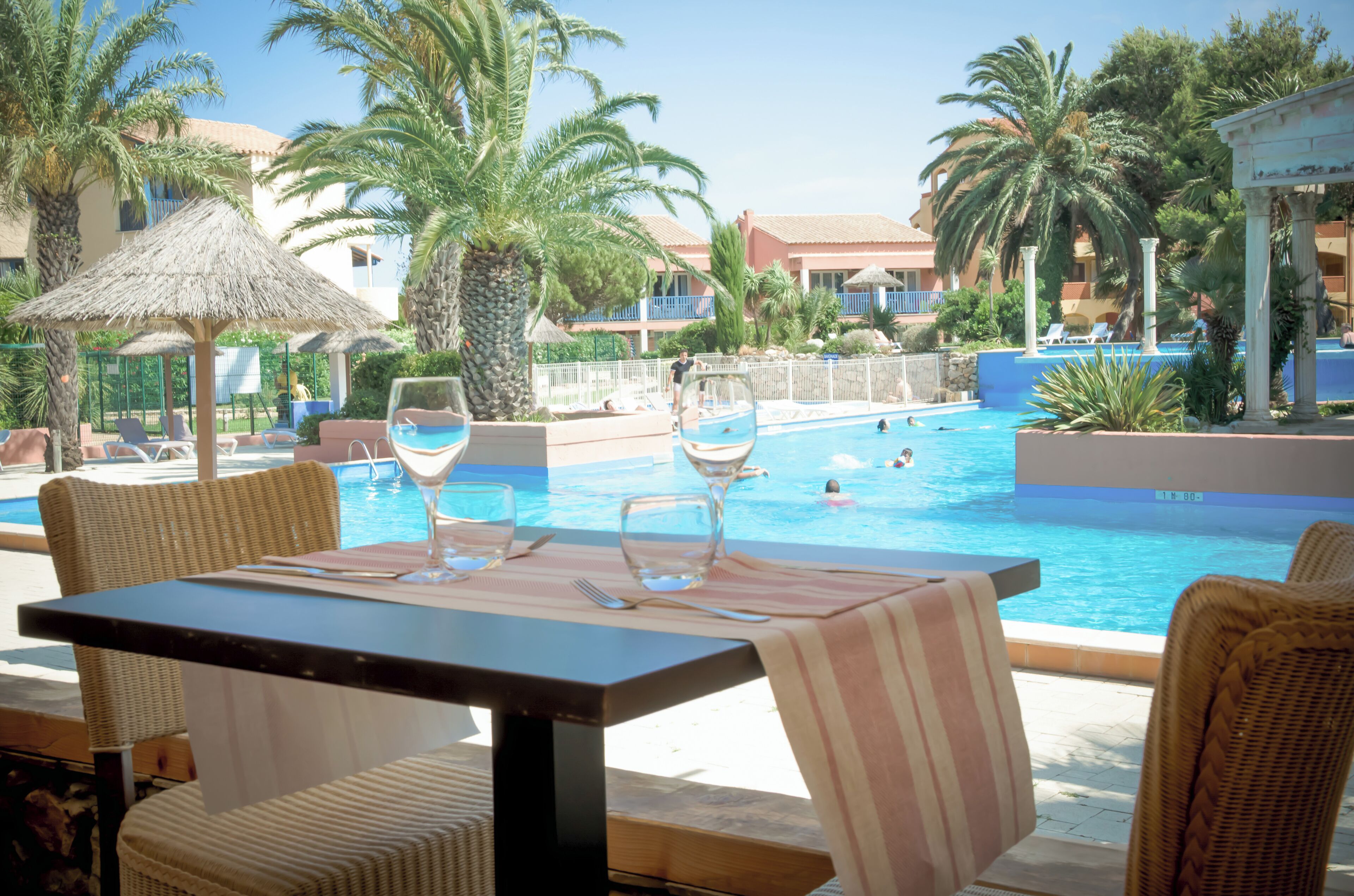 A poolside dining area with a table set for two, overlooking a swimming pool.