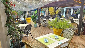 An outdoor patio area with wooden flooring, wicker furniture, and potted plants. - Malibu Village (Canet-en-Roussillon)
