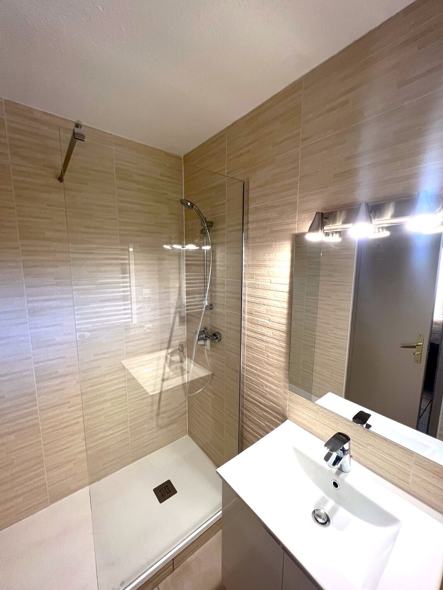 A modern bathroom with a glass-enclosed shower, a white sink, and a large mirror.