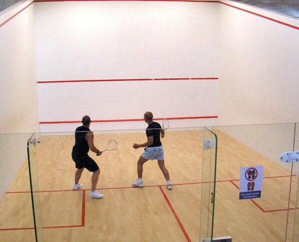 A squash court with a wooden floor, glass barriers, and a red line marking the court. - Malibu Village (Canet-en-Roussillon)