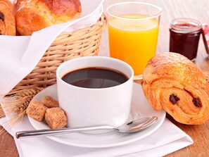 A breakfast setting with croissants, a cup of coffee, and a glass of orange juice on a wooden table. - Malibu Village (Canet-en-Roussillon)