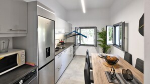 Una cocina moderna con electrodomésticos de acero inoxidable, un comedor con mesa de madera y vistas a la vegetación a través de un ventanal.