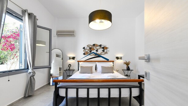Un dormitorio moderno con cama, mesitas de noche, una lámpara colgante y vistas al exterior.