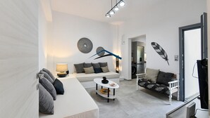 Una sala moderna con un sofá blanco, una mesita de centro pequeña y una lámpara decorativa. Hay un comedor con una mesa y sillas blancas. La habitación presenta un diseño minimalista, con un ventanal grande y una puerta que da a otra estancia.