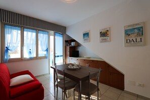 A compact living space with a dining area, a red armchair, and a kitchen with a counter and cabinets. - Modern two room apartment near the sea (Bibione)