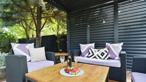 An outdoor seating area with wicker furniture, a wooden table, and a bottle of wine. - Stay at Puhara - Parklands Escape (Christchurch)
