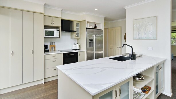 A modern kitchen with white cabinetry, a stainless steel refrigerator, a microwave, and a sink. - Stay at Puhara - Parklands Escape (Christchurch)
