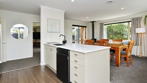 A modern kitchen with a central island, wooden dining table, and chairs. - Stay at Puhara - Parklands Escape (Christchurch)