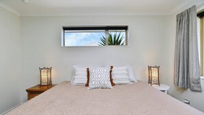 A bedroom with a large bed, two bedside tables, a window with a view, and a curtain. - Stay at Puhara - Parklands Escape (Christchurch)