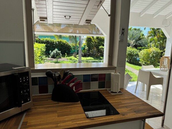 A kitchen with a wooden countertop, a microwave, a stove, and a window overlooking a garden. - COTE PLAGE LE BALAOU (Saint-François)