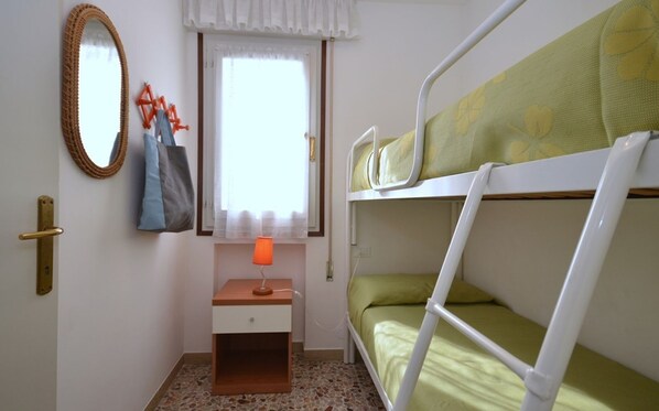 A bunk bed room with a window, a desk with a lamp, a mirror, and a door.