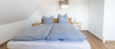 A neatly made bed with a wooden frame and blue bedding, two bedside tables with lamps, and a framed picture on the wall.