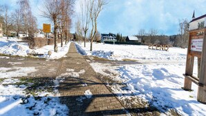 A snow-covered pathway leading to a building with a signboard. - Forest Villa With Sauna (Oberharz am Brocken)