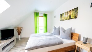 A modern bedroom with a wooden bed, a TV on a wooden stand, a bedside table with a lamp, and a painting on the wall. - Forest Villa With Sauna (Oberharz am Brocken)