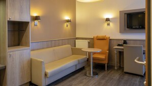 A modern room with a sofa, a small round table, a chair, and a TV mounted on the wall. - Blanckthys Hotel (Voeren)