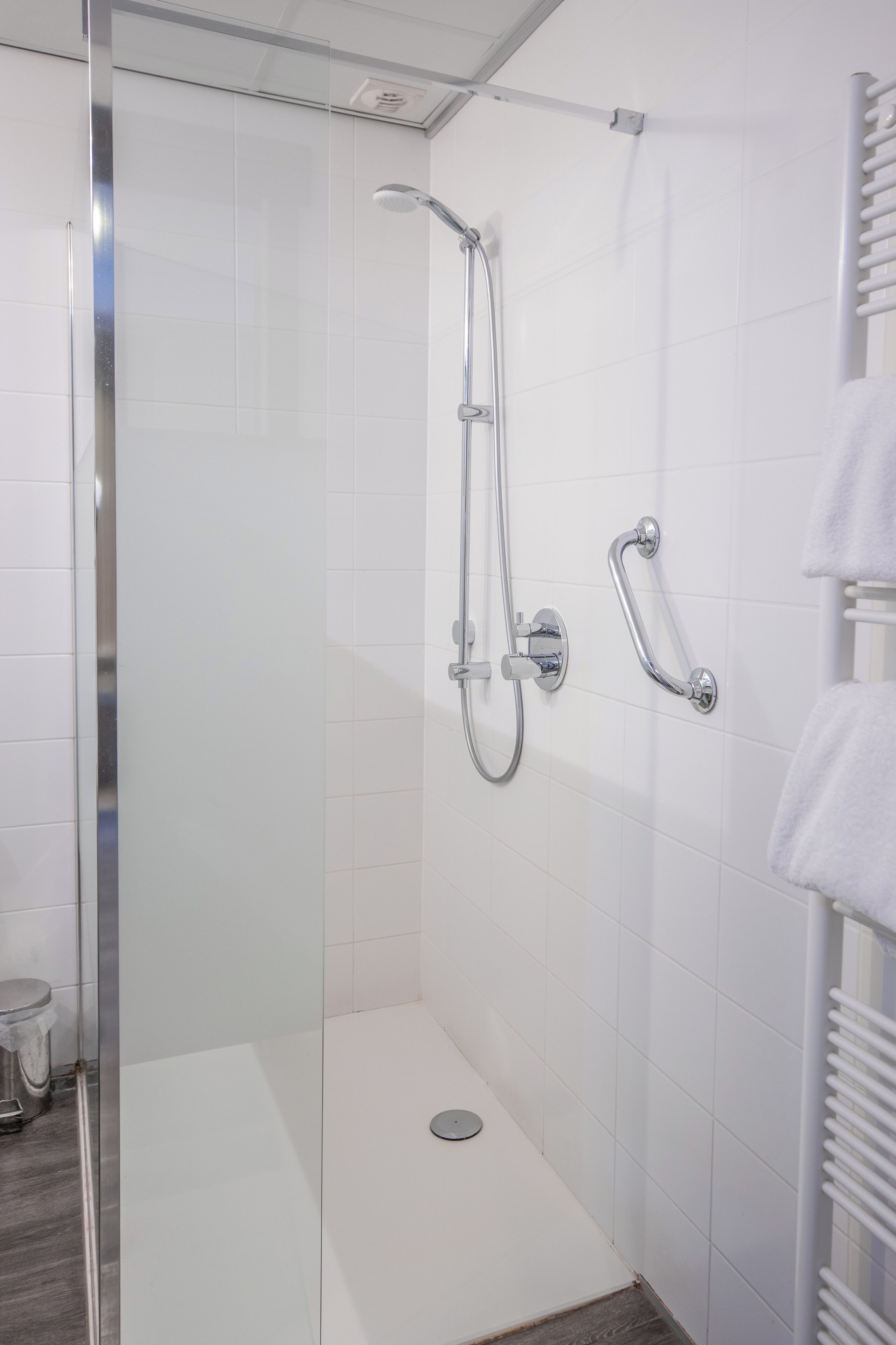 A modern bathroom with a glass-enclosed shower, a handheld showerhead, a wall-mounted towel rack, and a toilet.