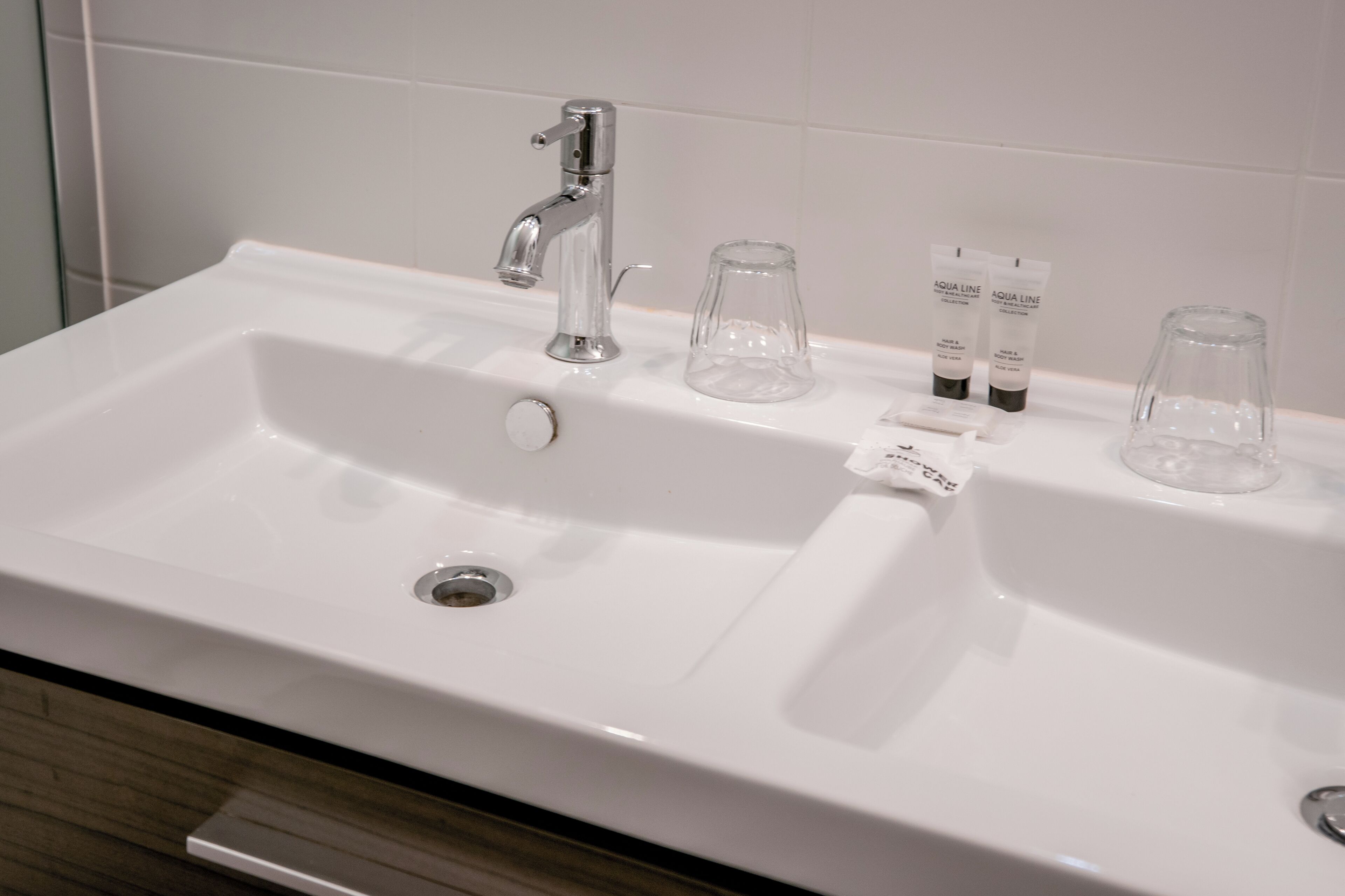 A white bathroom sink with a modern faucet, two glass bottles, and a soap dispenser.