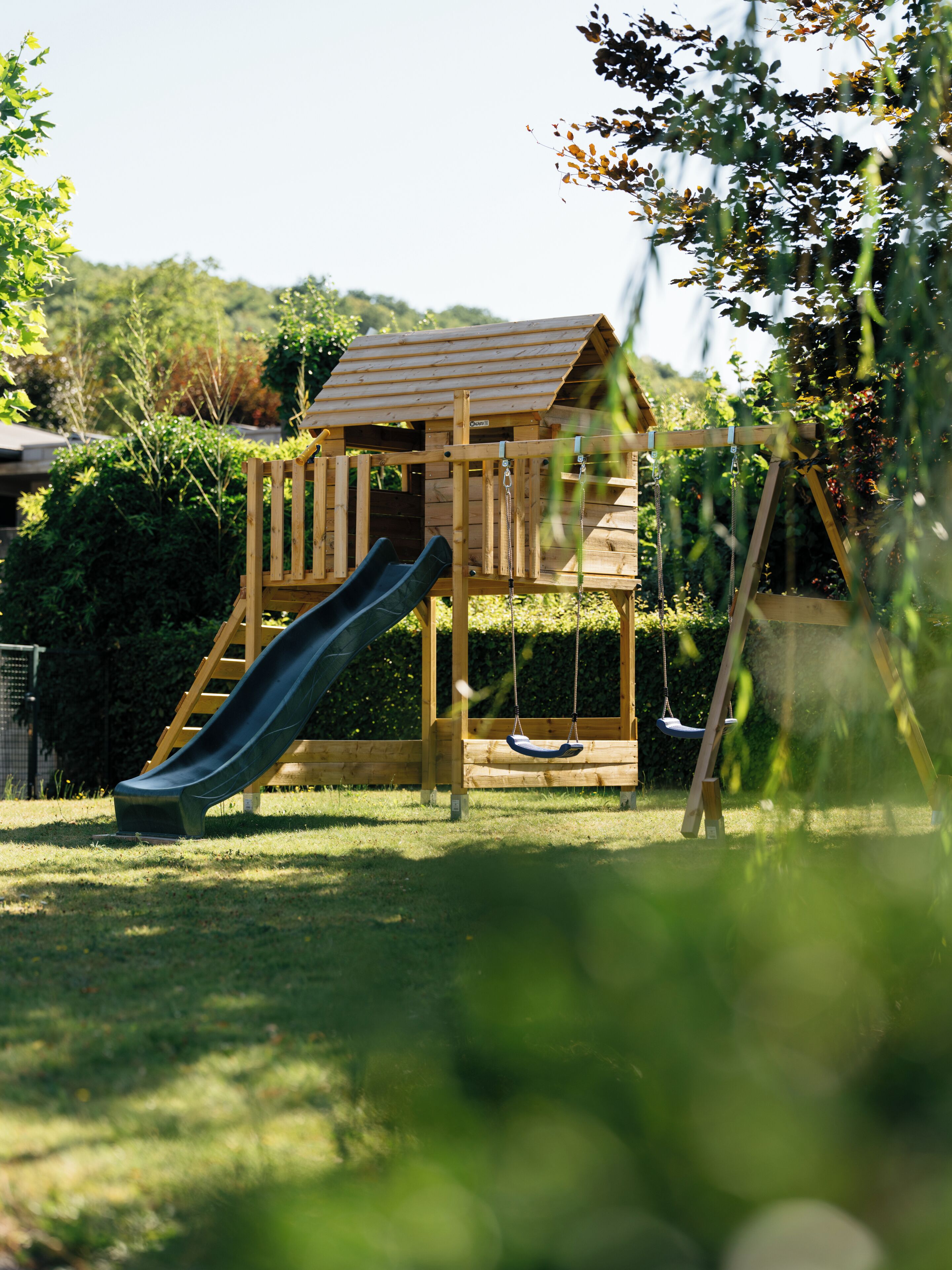 Estructura de madera para juegos con un tobogán y columpios en un patio cubierto de césped.