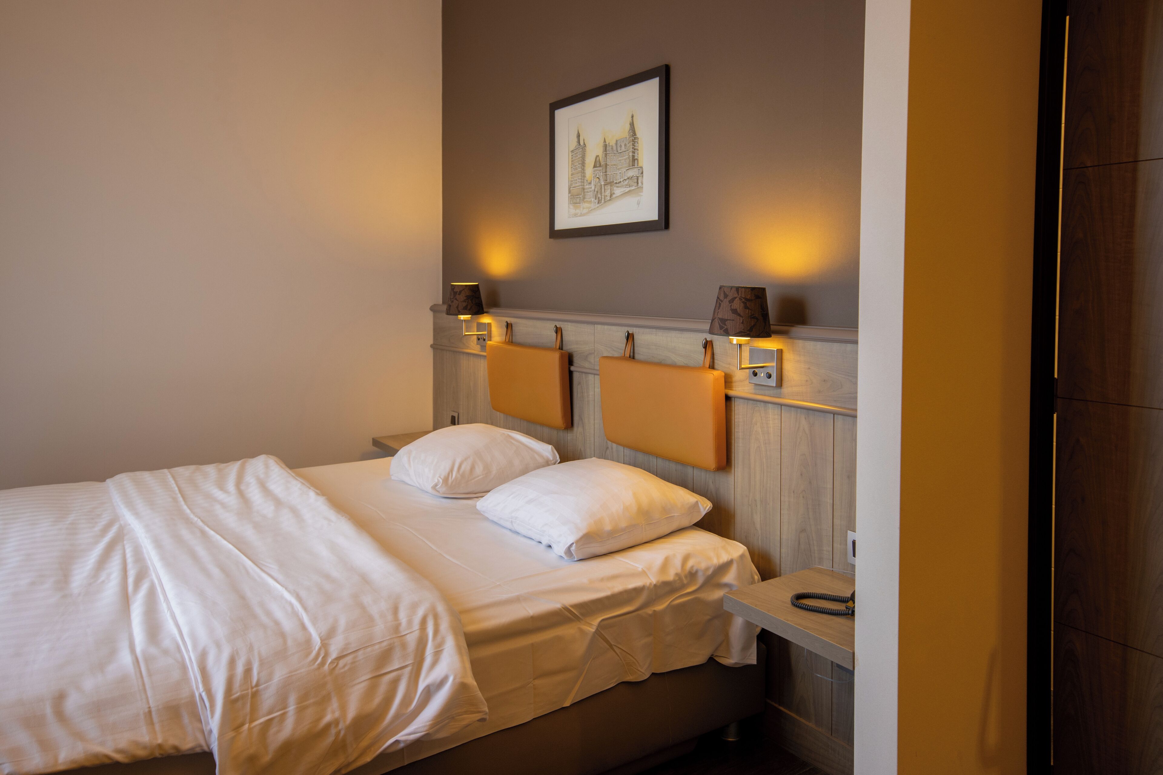 A neatly made bed with white linens, a headboard with integrated lighting, and a framed picture on the wall.