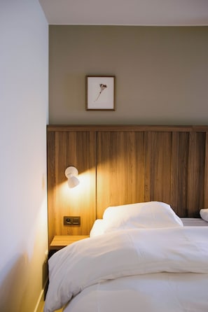 A hotel room with a wooden headboard, a bedside lamp, a framed picture on the wall, and a neatly made bed. - Blanckthys Hotel (Voeren)