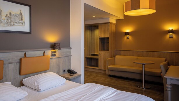 A hotel room with a bed, a sofa, a small table, and a wall-mounted lamp. - Blanckthys Hotel (Voeren)