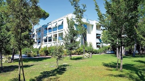 A modern building with multiple balconies, surrounded by a well-maintained grassy area with trees. - Contemporary flat near the sea with swimming pool (Bibione)