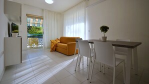A modern living room with a sofa, dining table, chairs, and a TV. - Contemporary flat near the sea with swimming pool (Bibione)