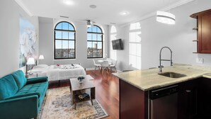 A modern living room with a teal sofa, a coffee table, and a dining area with a white table and chairs. There is a kitchen with a sink and a dishwasher. - XL Studio - Metro Studio, Chic Stay (Philadelphia)