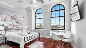 A bedroom with a bed, a desk, chairs, a painting, and large windows. - XL Studio - Metro Studio, Chic Stay (Philadelphia)