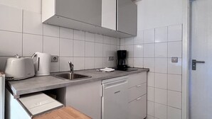Ett kompakt kök med vita skåp, en diskho, en kaffebryggare och en diskmaskin.