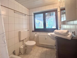 Un baño con inodoro, ventana con vistas, radiador y lavamanos con toalla.