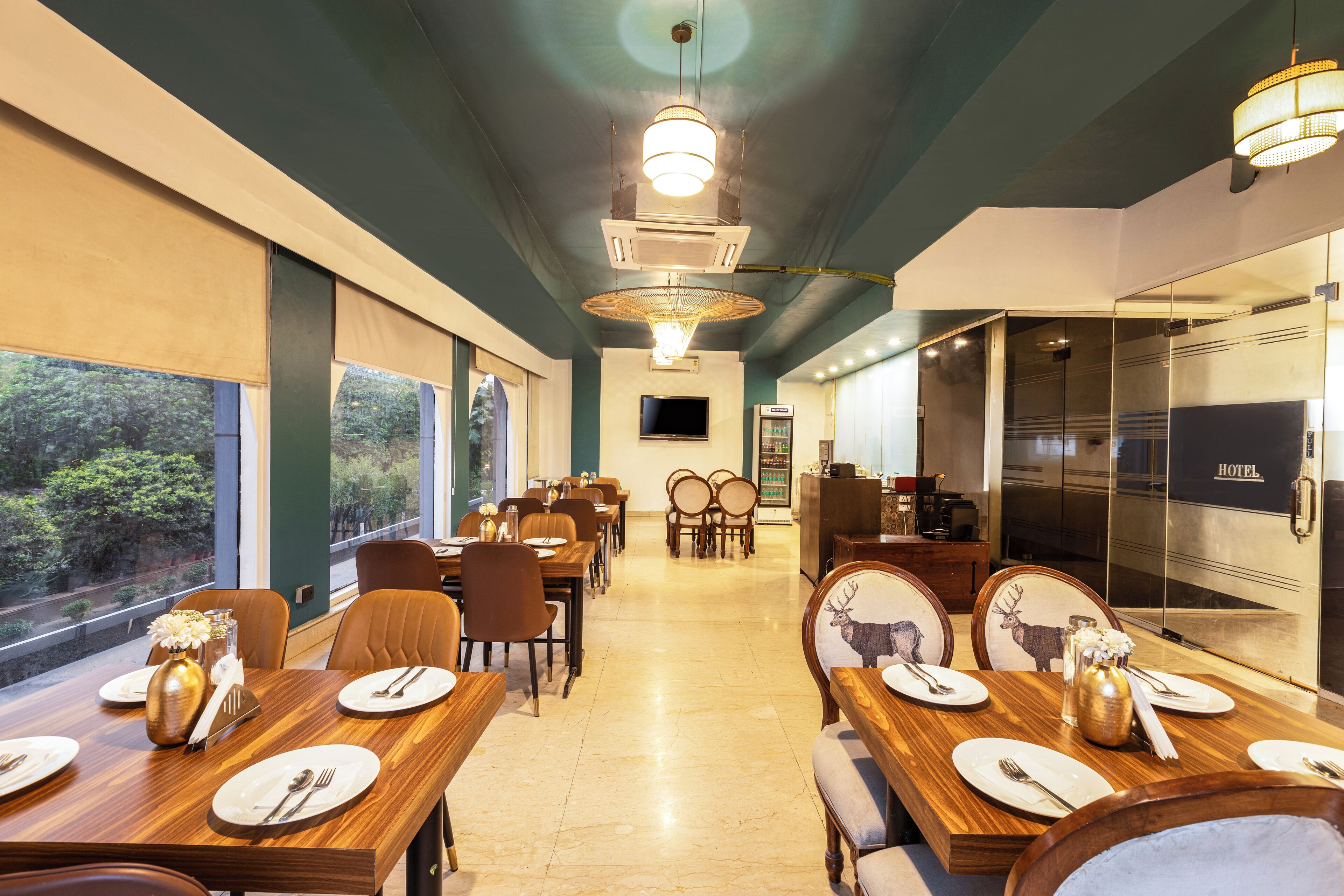 Een restaurantgedeelte in een hotel met gedekte tafels voor gasten, een televisiescherm en een minibars kastje.