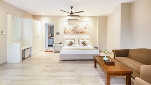 Una habitación de hotel moderna con una cama grande, un ventilador de techo, una mesita de noche, una mesa de centro y un sofá.