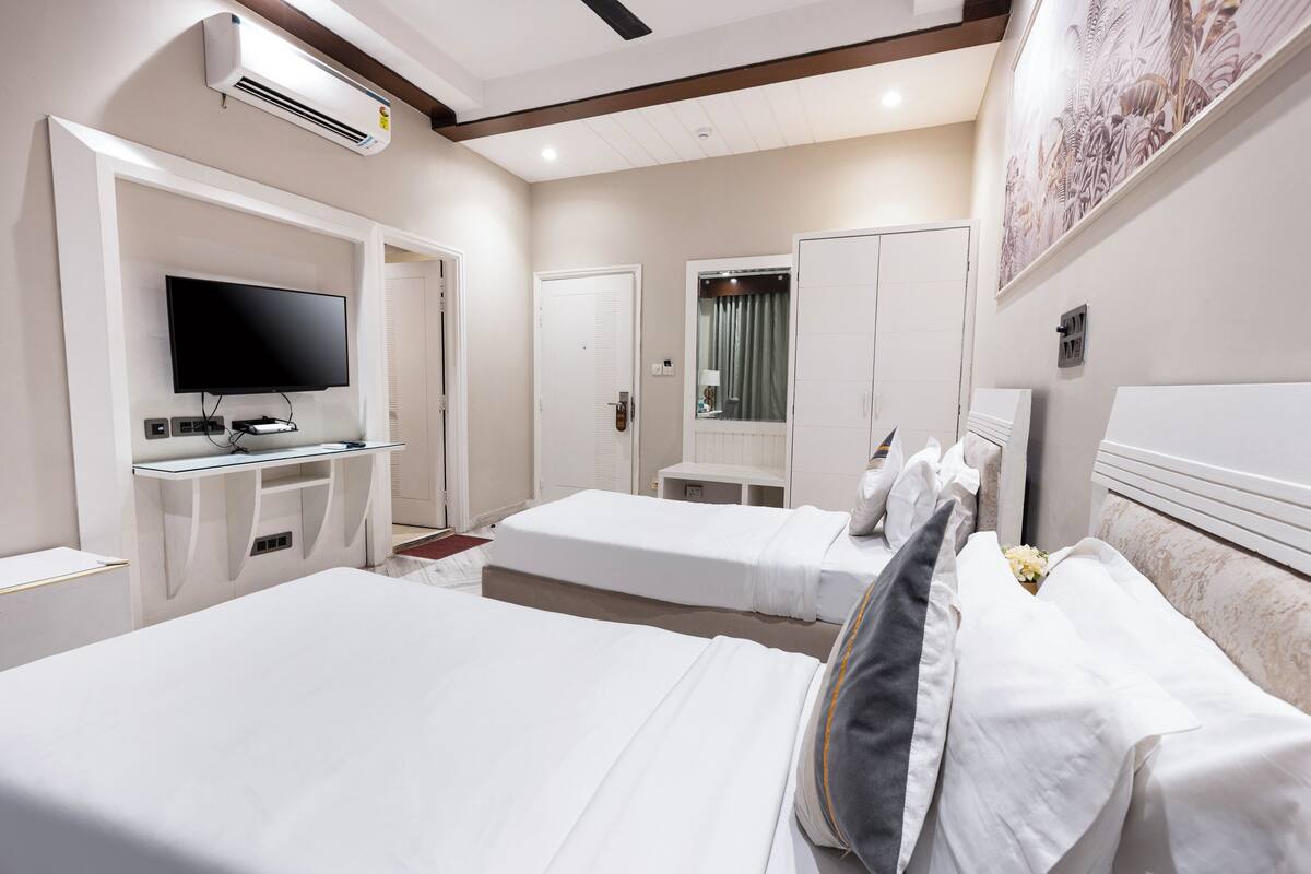 A hotel room with two beds, a TV, a desk, and a mirror.